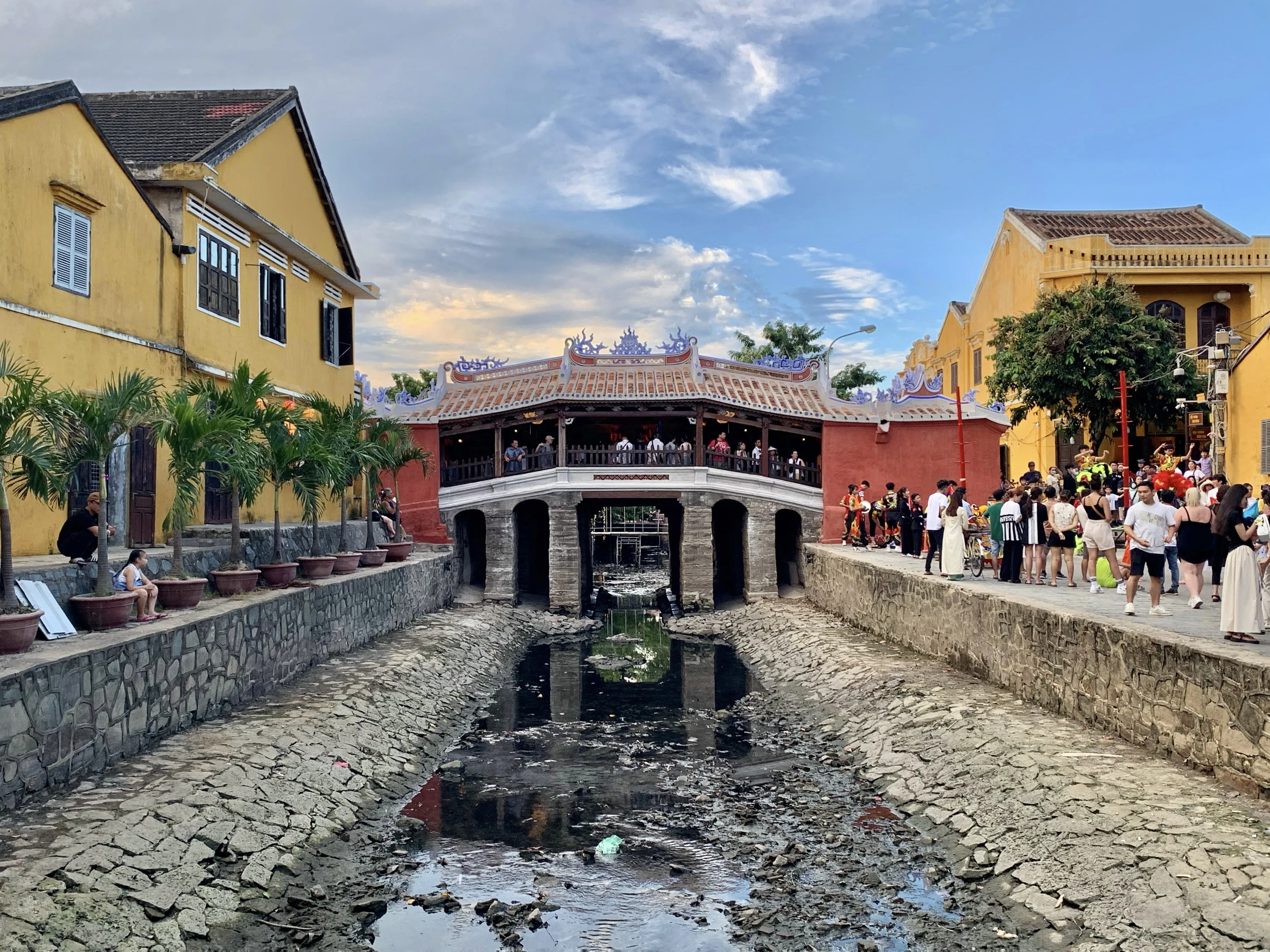 The Japanese Covered Bridge in Hoi An seen across a low creek, with a tiled roof and pink abutments