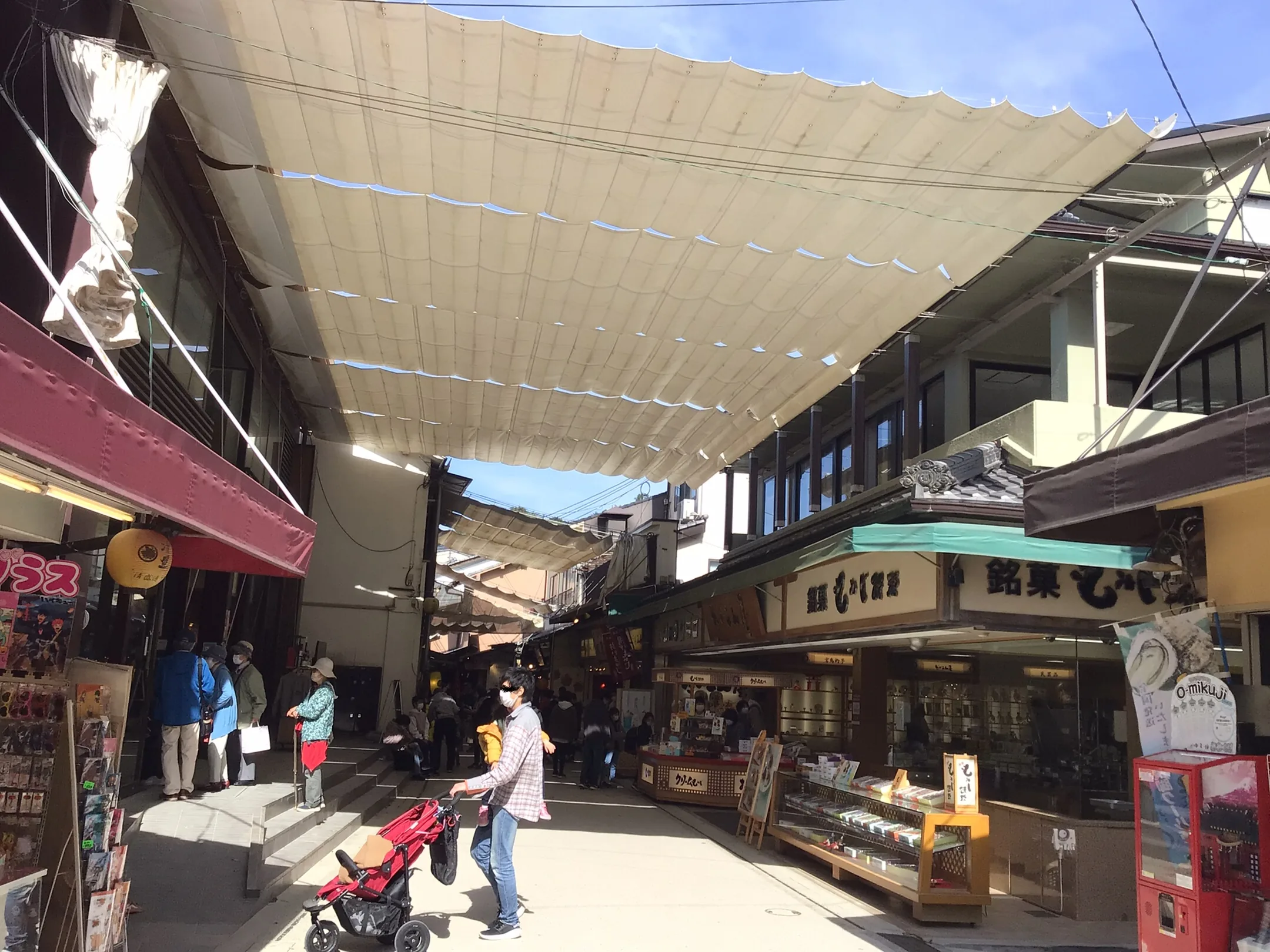 A covered shopping street on Miyajima, with canvas awnings, confectionery shops and people walking