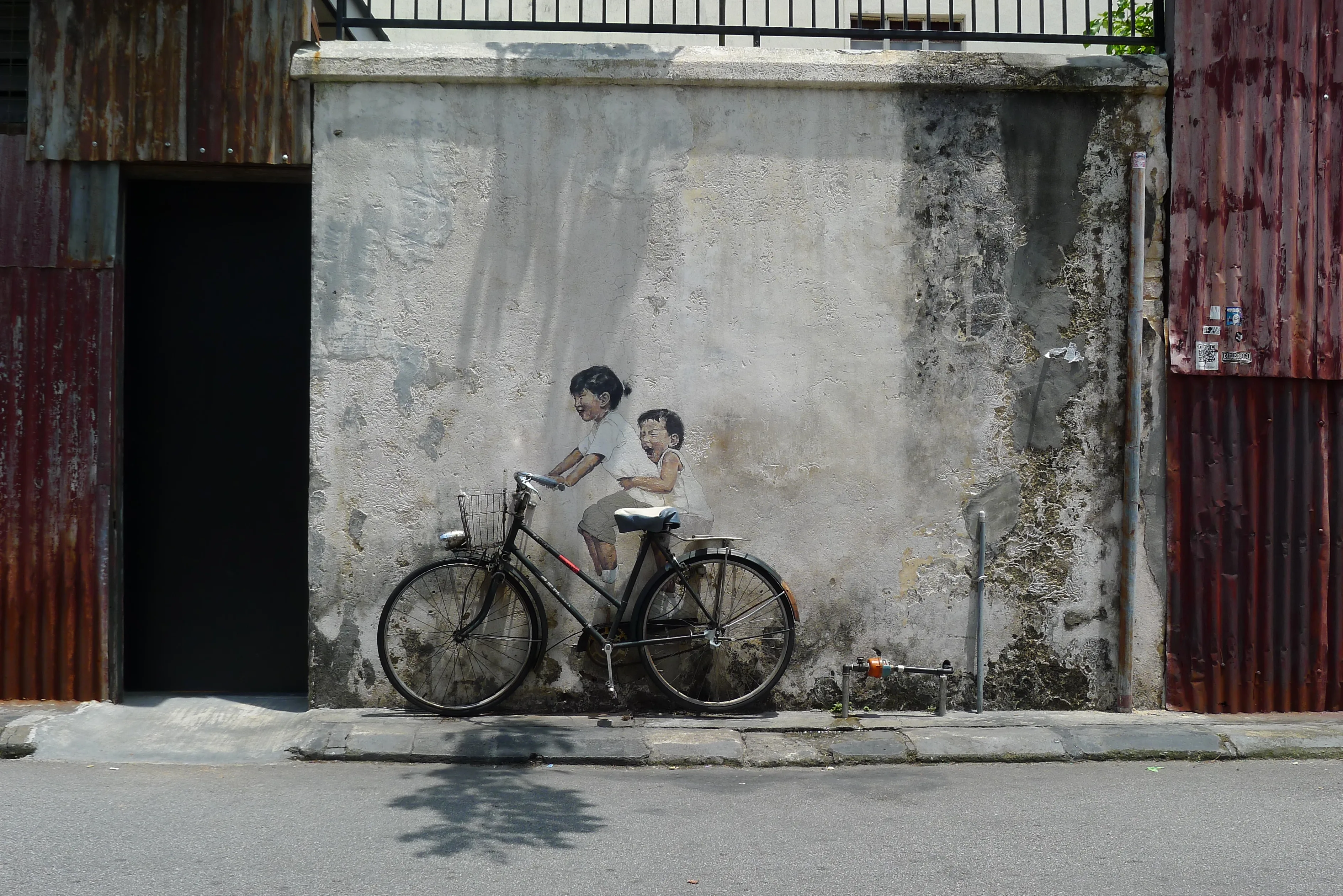 The Kids on Bicycle mural on a shophouse wall in Armenian Street, with a real bicycle standing in front