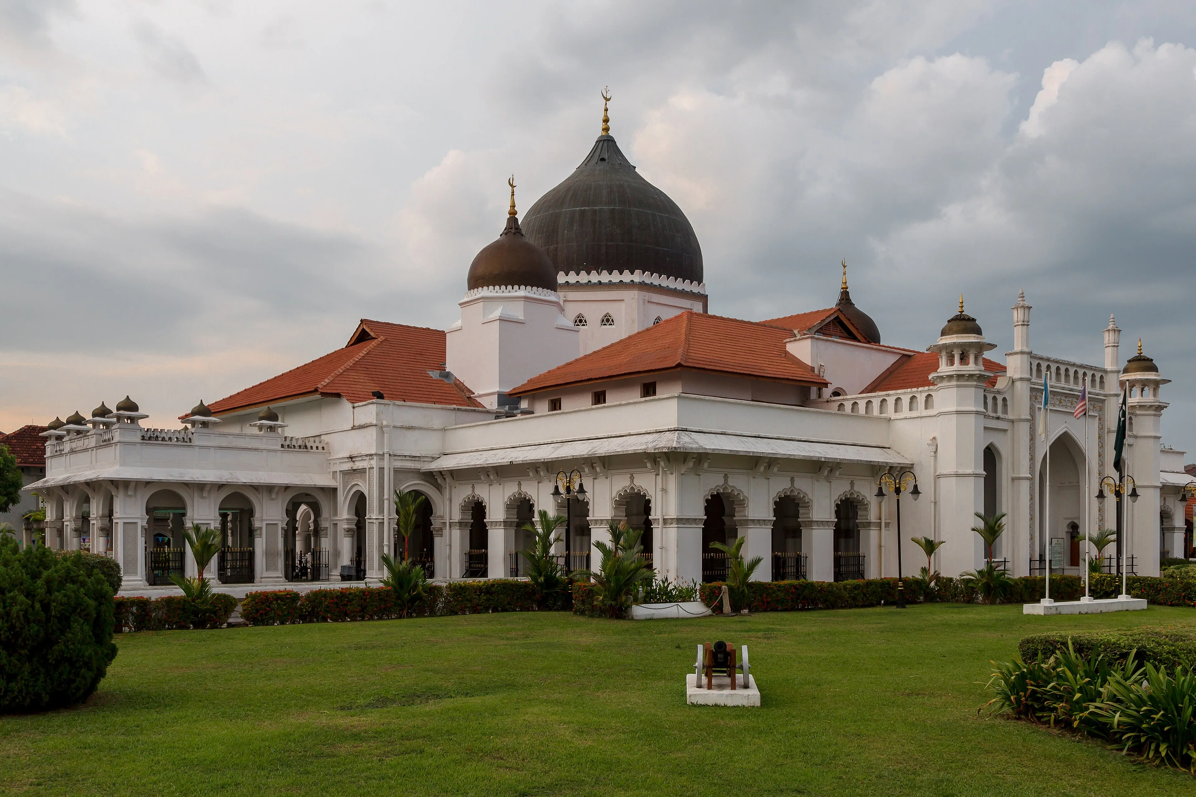 Kapitan Keling Mosque from its lawn, with white arcades, a dark dome and red-tiled roofs