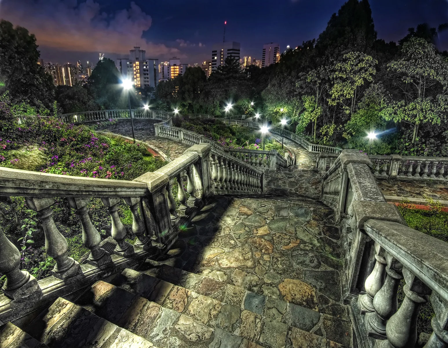 夜里弯曲的石台地和栏杆,树外是城市灯光